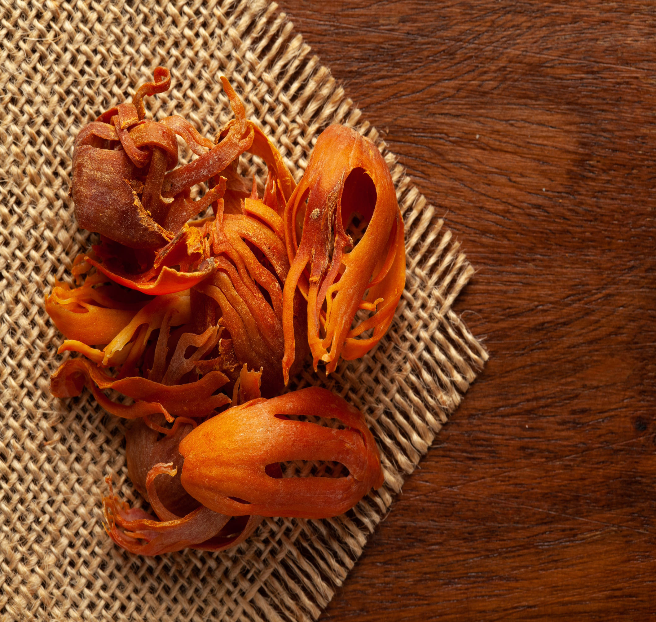 A close-up of dried mace, showcasing its vibrant red-orange color and delicate lace-like structure.
